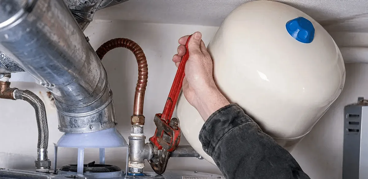 Water heater repair technician tightening plumbing connections near a tank unit in Houston, TX